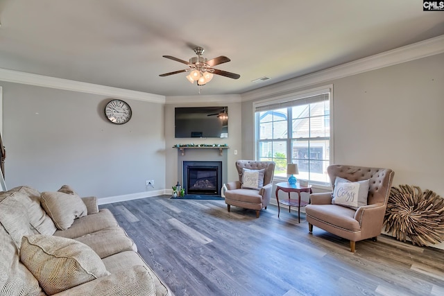 living room featuring ornamental molding, wood finished floors, a glass covered fireplace, ceiling fan, and baseboards