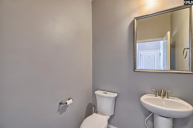 half bath featuring toilet, a sink, and baseboards