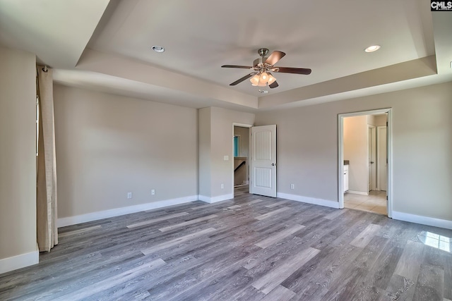 unfurnished bedroom with a raised ceiling, wood finished floors, baseboards, recessed lighting, and a ceiling fan