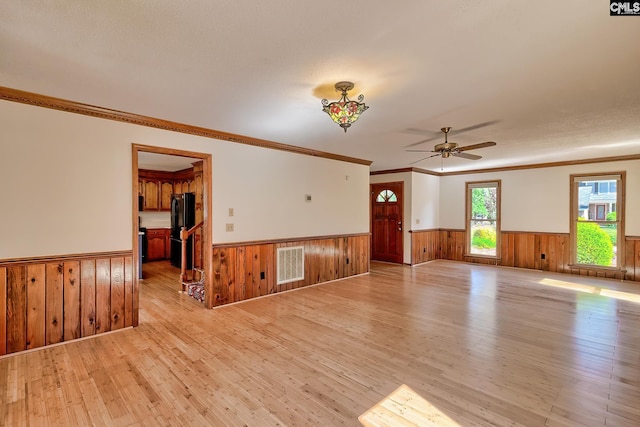 unfurnished room featuring wainscoting, light wood finished floors, wooden walls, ceiling fan, and ornamental molding