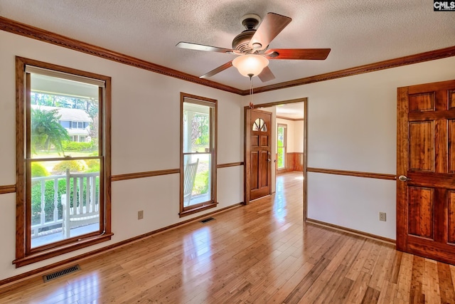 spare room featuring light wood-style flooring, a textured ceiling, baseboards, a ceiling fan, and crown molding