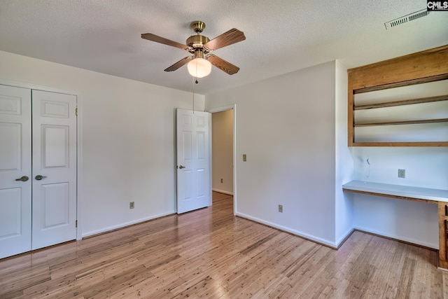 unfurnished bedroom featuring light wood-type flooring, a closet, baseboards, an office area, and a textured ceiling