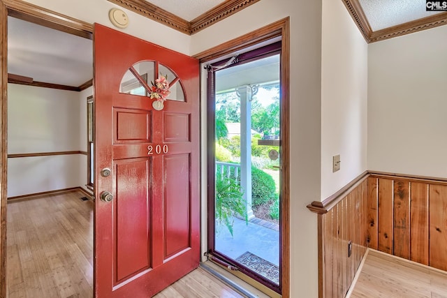 entrance foyer featuring crown molding, light wood finished floors, a wainscoted wall, and wooden walls