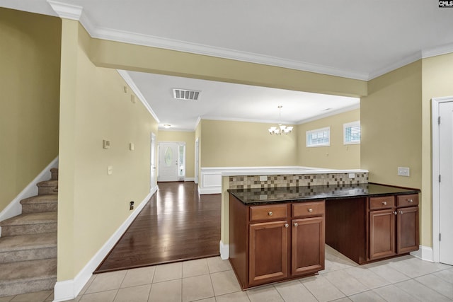 kitchen featuring a chandelier, crown molding, a peninsula, dark stone countertops, and decorative light fixtures