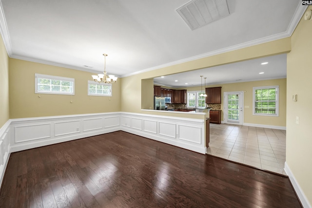 empty room with crown molding, a chandelier, wood finished floors, healthy amount of natural light, and recessed lighting