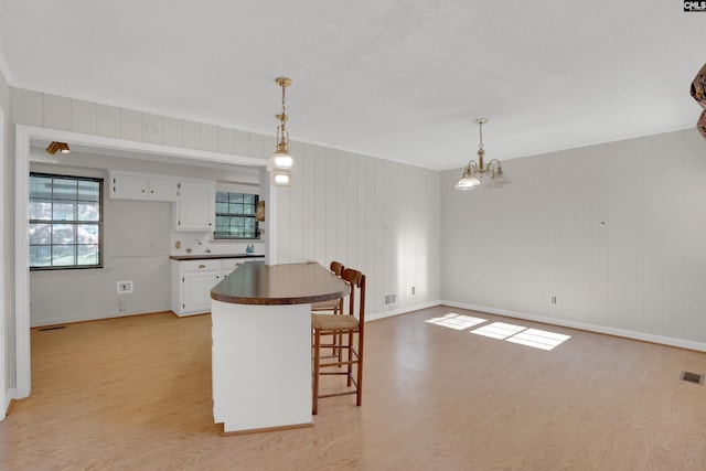 604 Shady Ln, Cayce, SC 29033 - kitchen with light wood-type flooring, dark countertops, white cabinetry, a breakfast bar, and ornamental molding