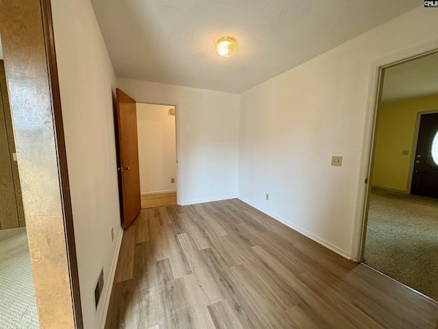 empty room with wood finished floors, a textured ceiling, and baseboards