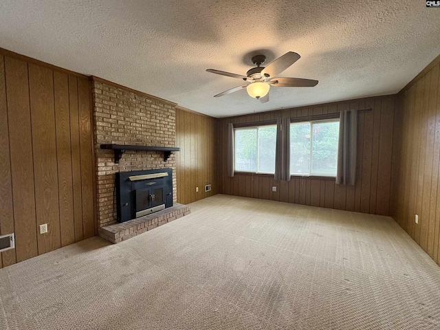 unfurnished living room with ceiling fan, wooden walls, light carpet, a brick fireplace, and a textured ceiling