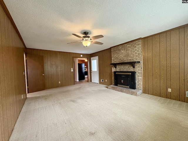 unfurnished living room with ceiling fan, wooden walls, light colored carpet, a textured ceiling, and a fireplace