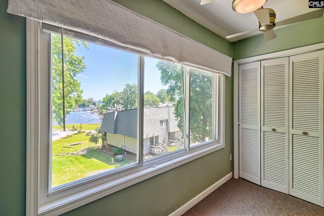 unfurnished bedroom with a water view, carpet floors, a closet, baseboards, and a ceiling fan