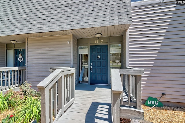 entrance to property with covered porch and a shingled roof