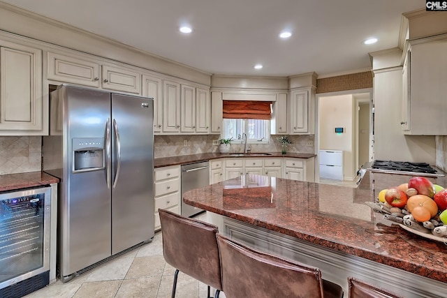 kitchen with appliances with stainless steel finishes, beverage cooler, a sink, ornamental molding, and dark stone countertops