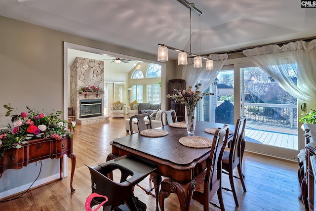 dining room with a ceiling fan, healthy amount of natural light, a fireplace, wood finished floors, and vaulted ceiling