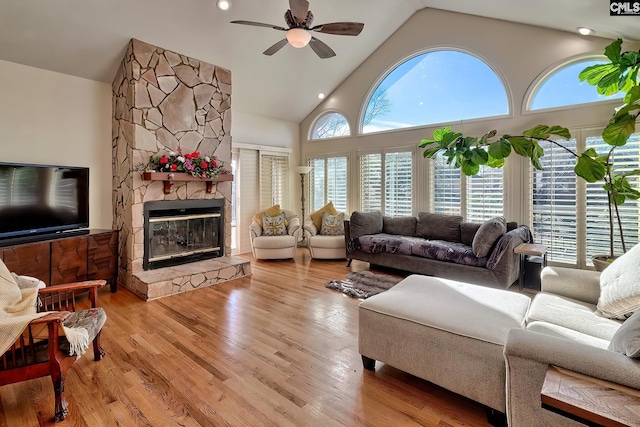 living room featuring a ceiling fan, high vaulted ceiling, a stone fireplace, and wood finished floors
