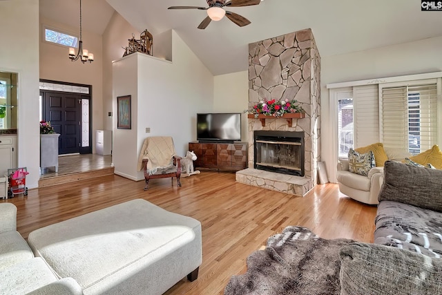 living area with high vaulted ceiling, a stone fireplace, wood finished floors, ceiling fan, and a chandelier
