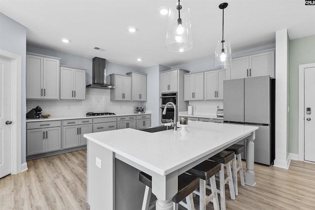 kitchen with appliances with stainless steel finishes, wall chimney exhaust hood, a sink, light wood finished floors, and gray cabinetry