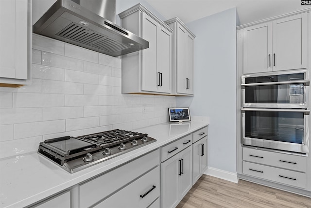 kitchen featuring wall chimney exhaust hood, appliances with stainless steel finishes, light countertops, and decorative backsplash
