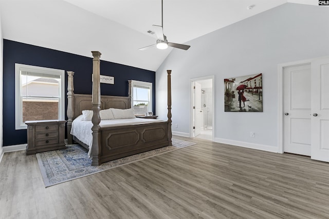 bedroom featuring high vaulted ceiling, wood finished floors, baseboards, ensuite bath, and ornate columns