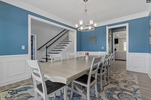 dining room featuring a chandelier, stairs, light wood finished floors, a wainscoted wall, and ornamental molding