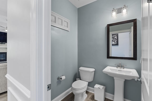 half bath featuring wood finished floors, toilet, and baseboards