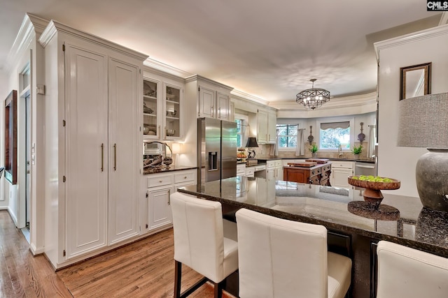 kitchen featuring stainless steel fridge, light wood-style flooring, crown molding, a chandelier, and a kitchen bar