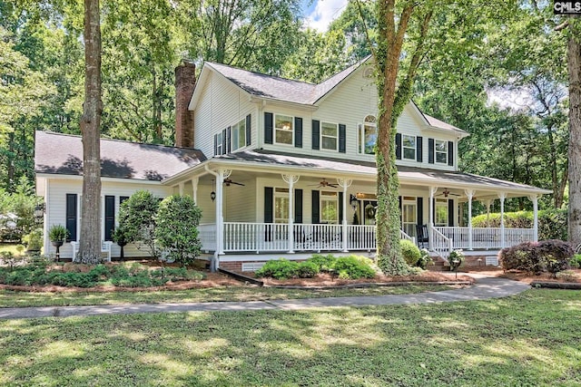 country-style home with ceiling fan, covered porch, a chimney, and a front yard