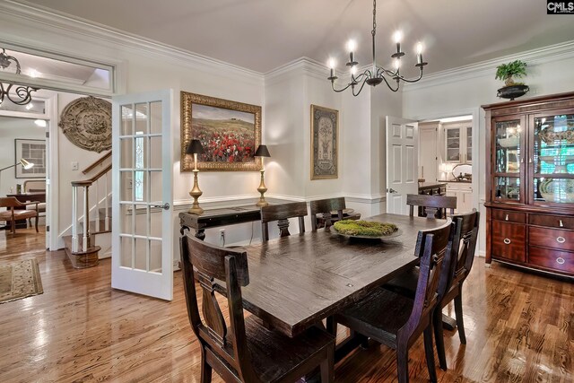 dining area featuring light wood-style flooring, ornamental molding, a chandelier, and stairs
