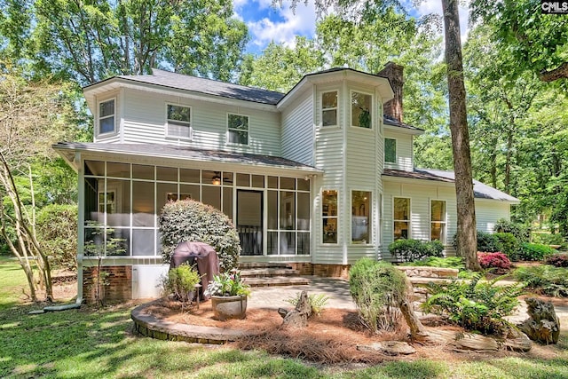 back of house featuring a sunroom, a chimney, a patio, and a shingled roof