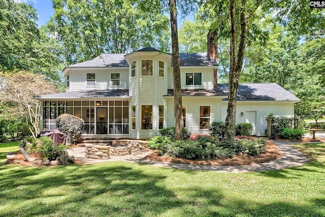 back of property featuring a chimney, a sunroom, a lawn, and a fire pit