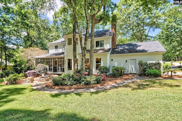back of property with a sunroom, a chimney, and a lawn