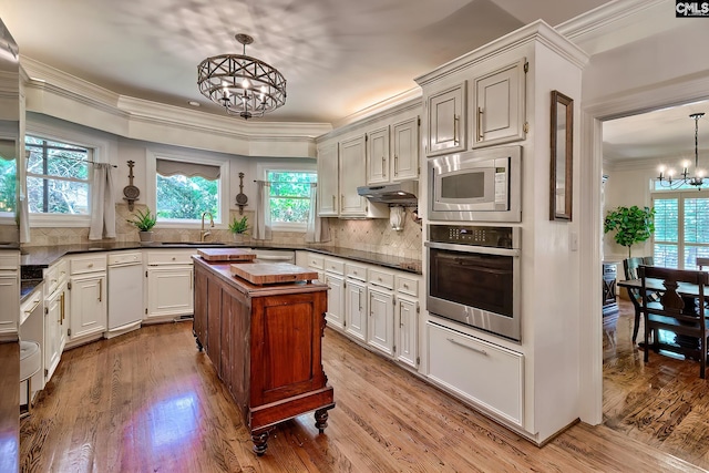 kitchen featuring stainless steel appliances, a chandelier, plenty of natural light, crown molding, and a sink
