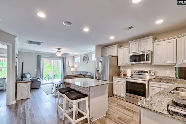 kitchen with stainless steel appliances, open floor plan, light wood-type flooring, a center island, and crown molding