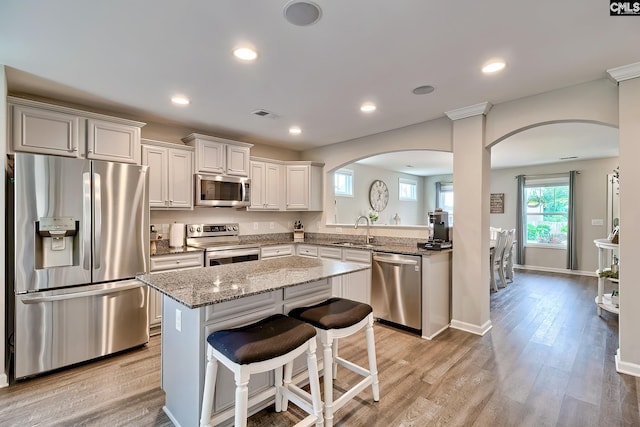 kitchen with appliances with stainless steel finishes, arched walkways, a sink, a kitchen island, and light wood finished floors