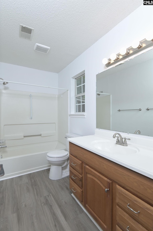 bathroom featuring wood finished floors, a textured ceiling, toilet, vanity, and bathtub / shower combination