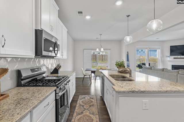 kitchen featuring appliances with stainless steel finishes, a sink, backsplash, white cabinetry, and a center island with sink