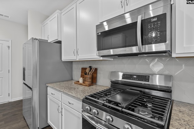 kitchen with stainless steel appliances, white cabinetry, backsplash, and light stone countertops