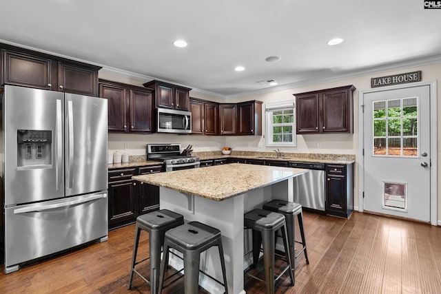 kitchen featuring stainless steel appliances, a sink, a kitchen breakfast bar, crown molding, and dark brown cabinetry