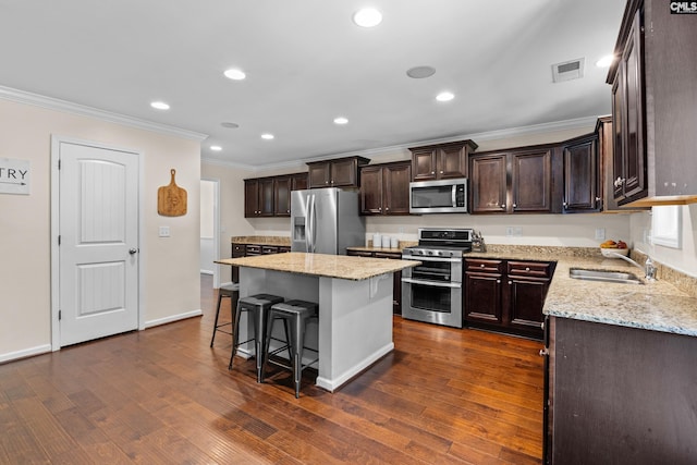kitchen with stainless steel appliances, a sink, crown molding, dark brown cabinets, and a kitchen bar