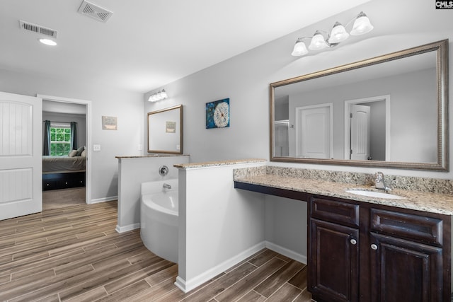 ensuite bathroom featuring wood finished floors, baseboards, a garden tub, and vanity