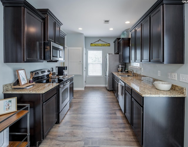 kitchen with appliances with stainless steel finishes, a sink, wood finished floors, light stone counters, and recessed lighting