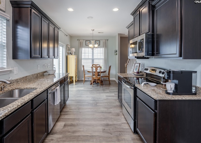 kitchen with stainless steel appliances, a sink, a chandelier, light wood finished floors, and light stone countertops