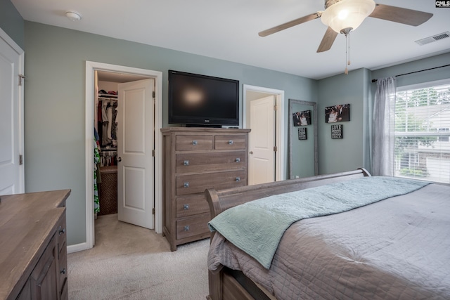 bedroom with a spacious closet, light colored carpet, a closet, ceiling fan, and baseboards