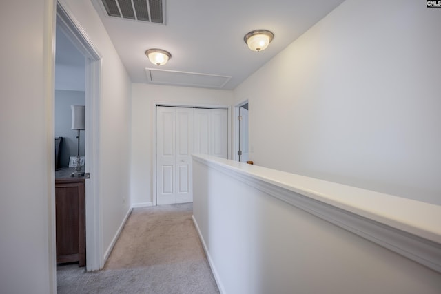 hallway featuring light colored carpet, baseboards, and attic access