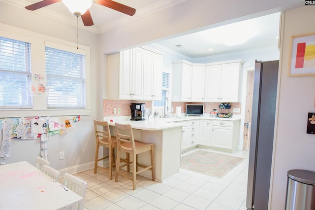 kitchen featuring freestanding refrigerator, a sink, healthy amount of natural light, backsplash, and ornamental molding