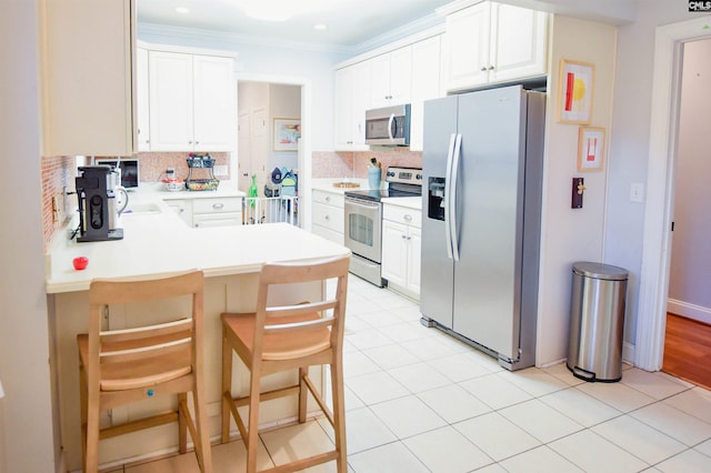 kitchen featuring stainless steel appliances, a peninsula, decorative backsplash, a breakfast bar area, and light countertops