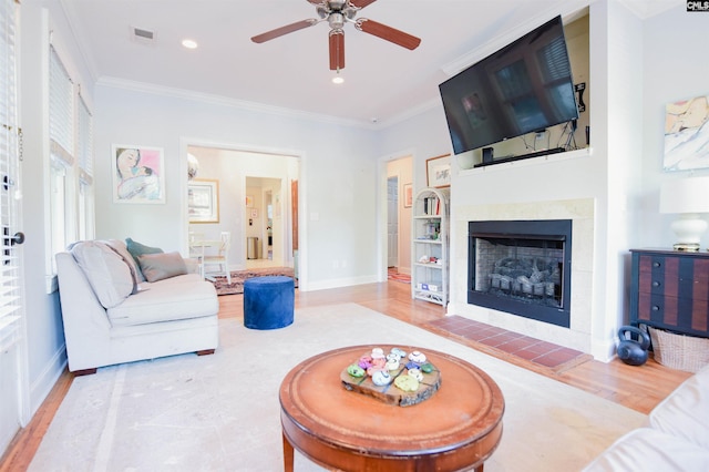 living area with ornamental molding, ceiling fan, wood finished floors, baseboards, and a tile fireplace