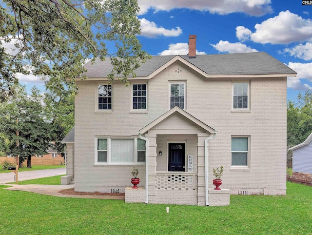 view of front of property with a front yard, brick siding, and a chimney