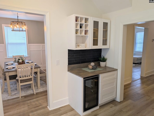 indoor bar featuring beverage cooler, a chandelier, light wood-style floors, healthy amount of natural light, and wainscoting