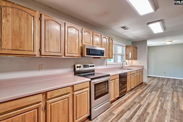 kitchen with appliances with stainless steel finishes, a sink, light wood finished floors, light countertops, and baseboards