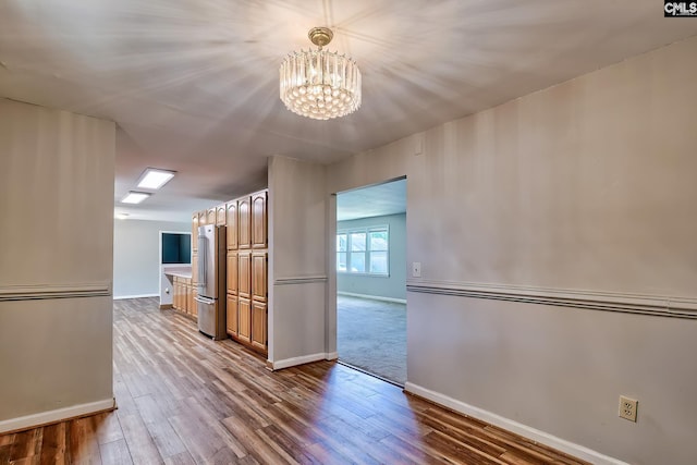 unfurnished room featuring a chandelier, baseboards, and wood finished floors